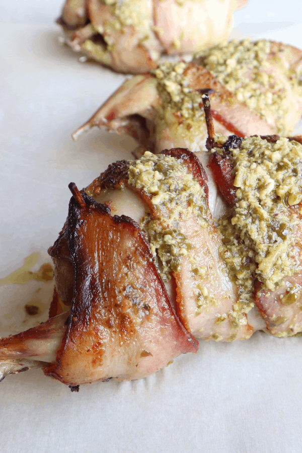 Bacon-wrapped stuffed quail on parchment, topped with garlic butter pesto