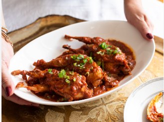 Quail braised in tomato sauce, served in a white dish and scattered with chopped herbs