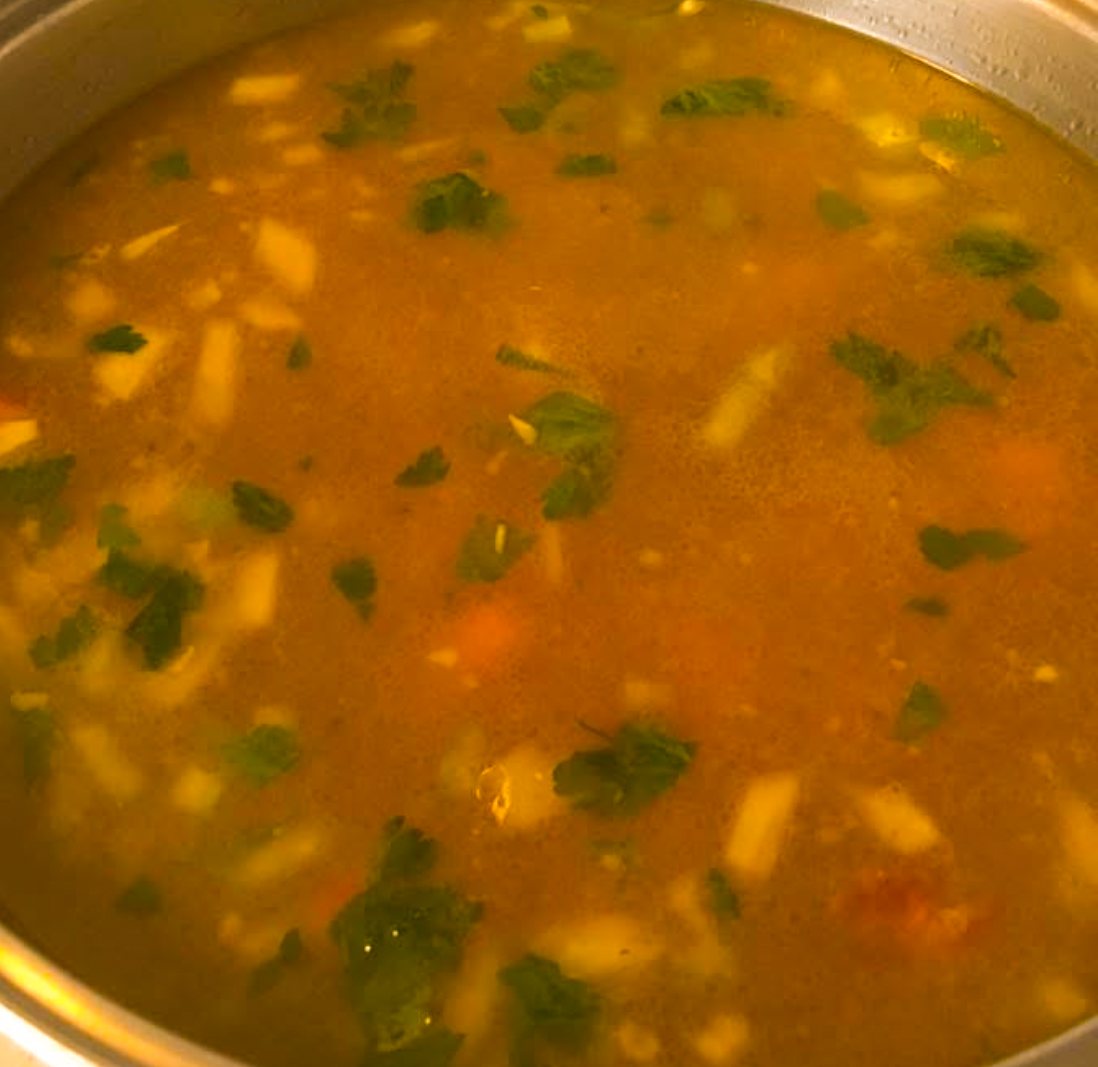 A pot of chicken vegetable soup with carrots, celery and fresh parsley leaves