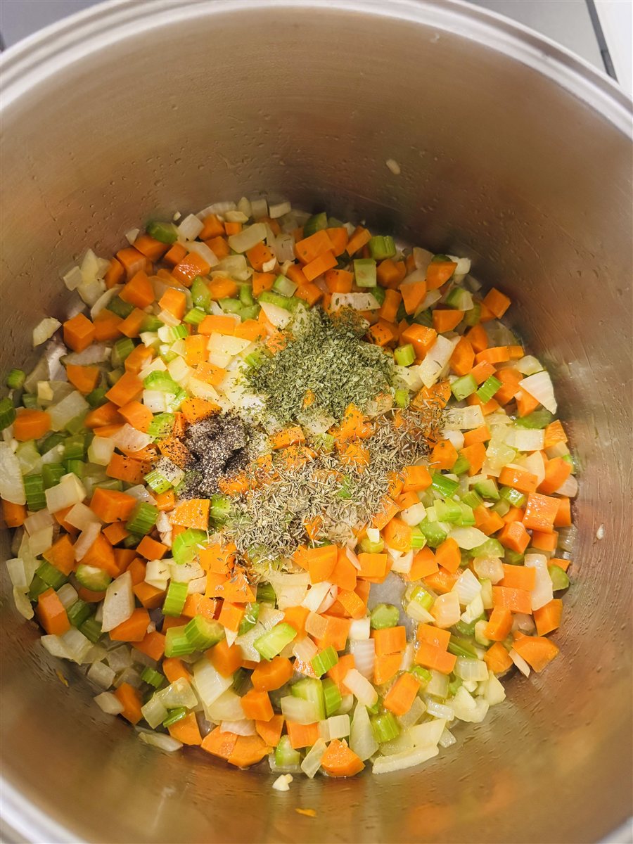 Dried herbs and black pepper on softened carrots, celery and onion in a soup pot